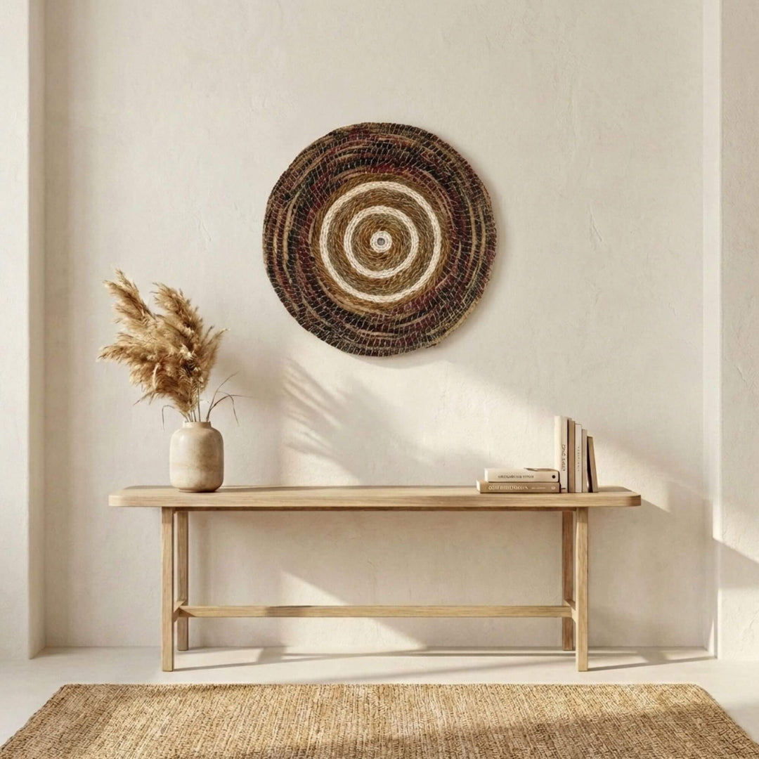 Woven Samara wall art piece above a wooden console table with a vase and books in a minimalistic room.