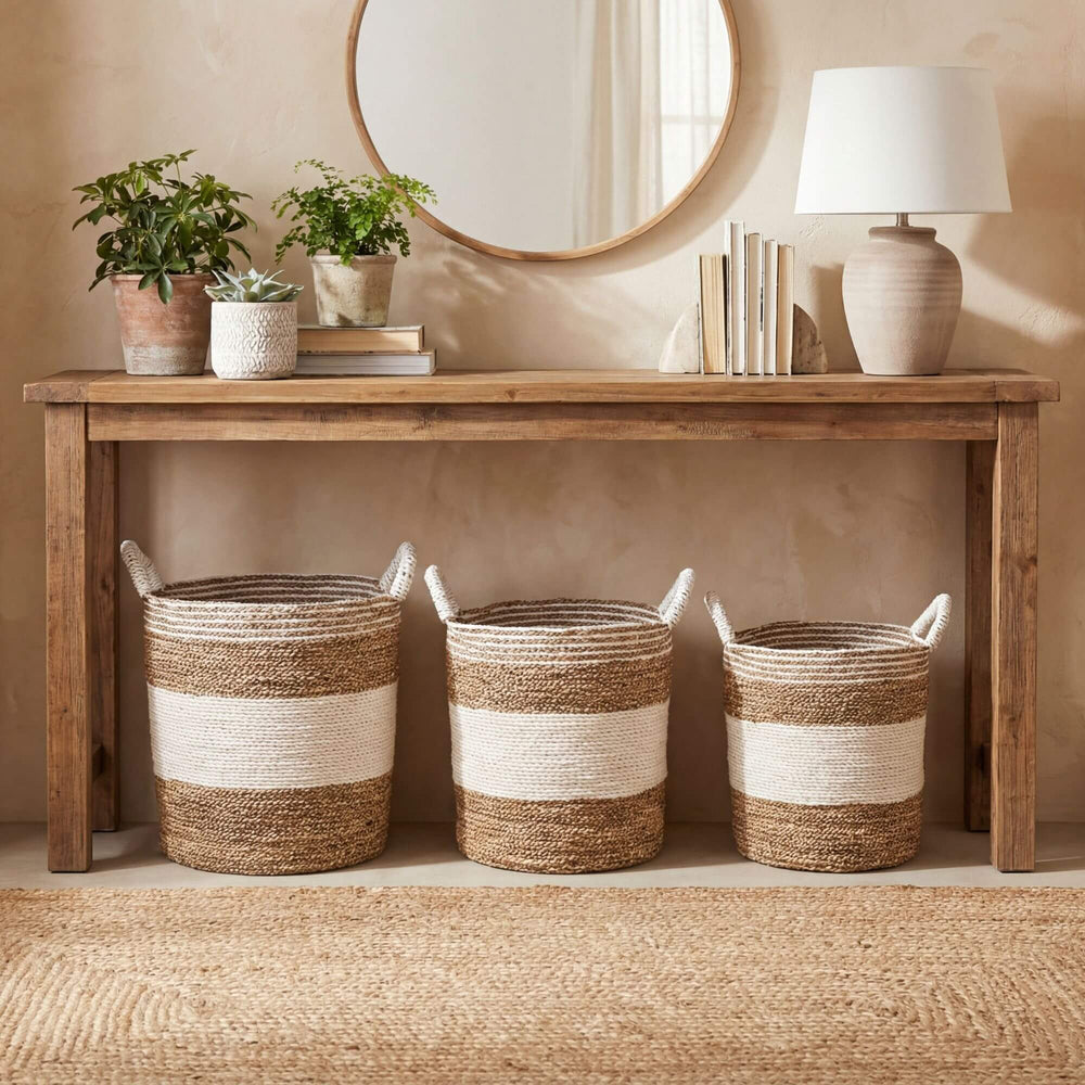 Wooden console table with decorative items including Sanblas seagrass baskets, plants, and a lamp against a beige wall.