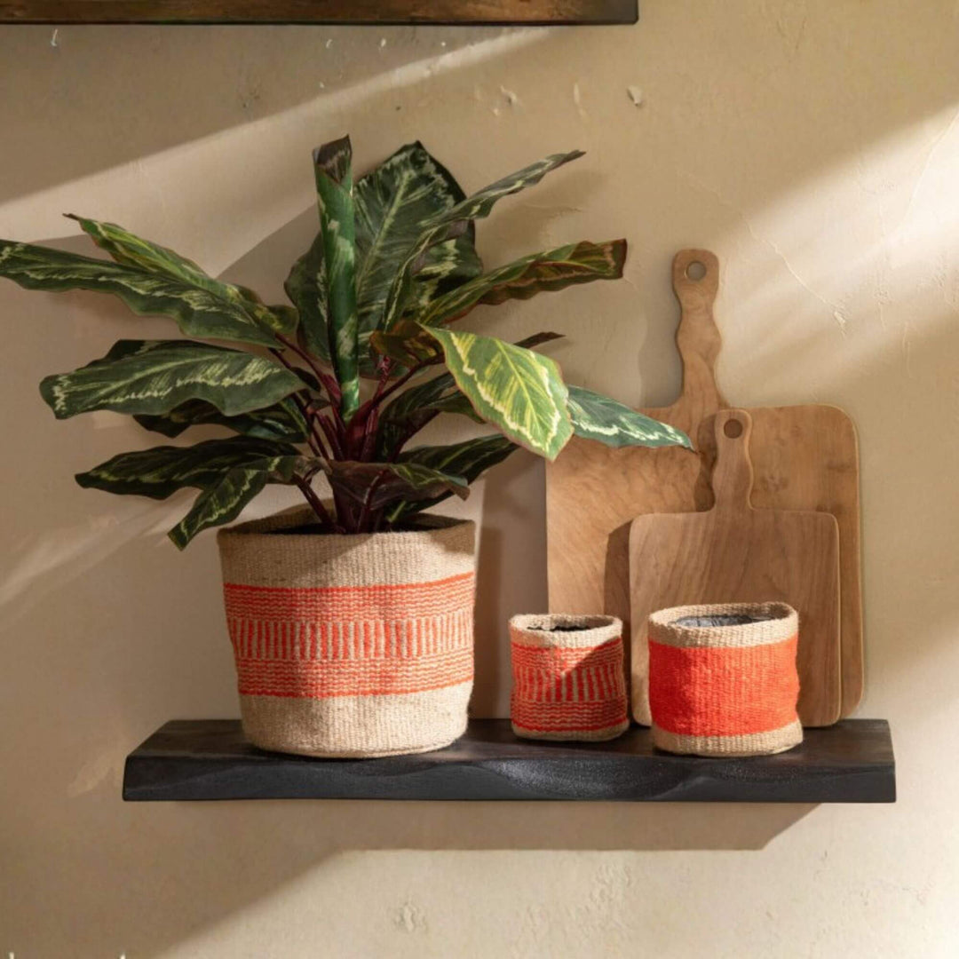 Pair of orange jute baskets used as planters on a shelf in a cozy interior.