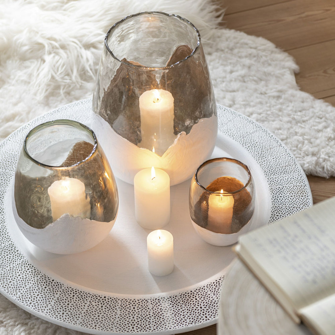 Cozy lifestyle scene featuring lit Snow Glass Candles on a tray with soft textiles.