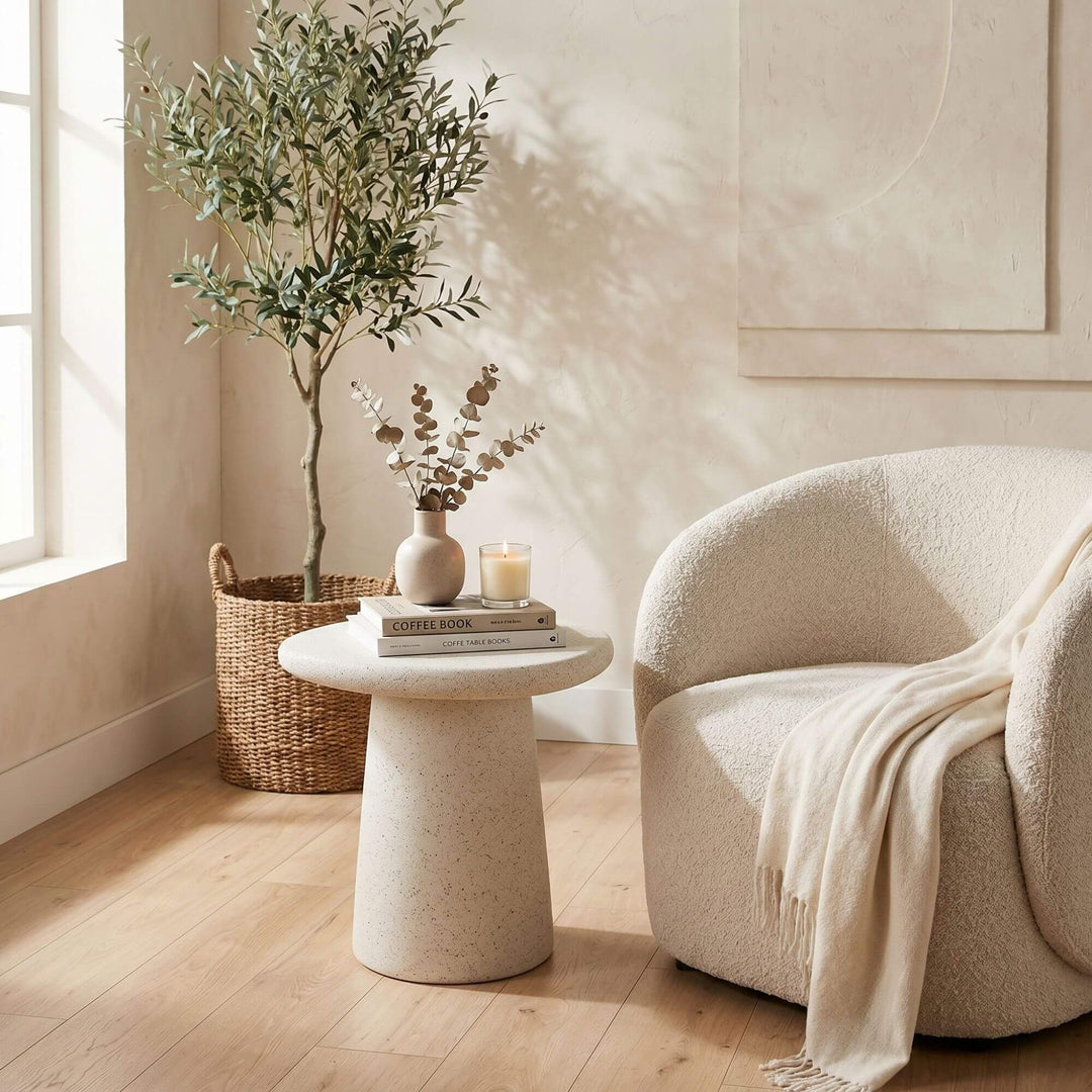 Modern interior with a beige armchair, round stone look outdoor side table, and decorative plants.