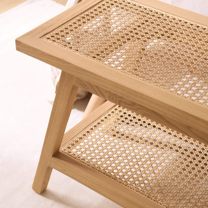 Close-up of the Senja bench showing the woven rattan surface, lower shelf, and angled sungkai wood legs