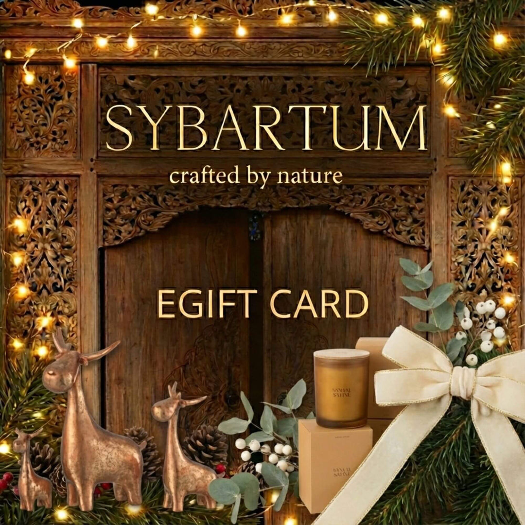 Christmas-themed Sybartum eGift Card design with carved wooden background, warm string lights, bronze reindeer figures, festive greenery, candle and large ivory bow.