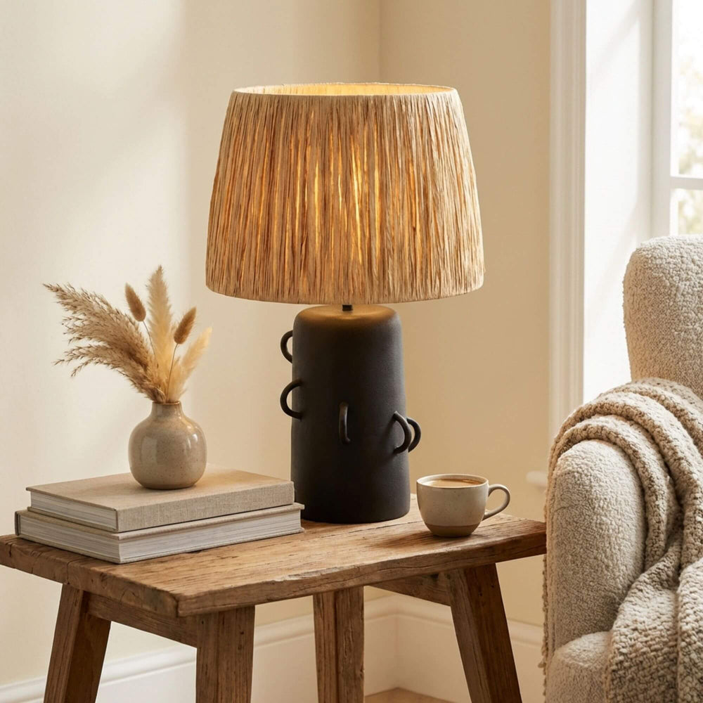 Decorative lamp on a wooden table with books, a vase, and a cup in a cozy room.