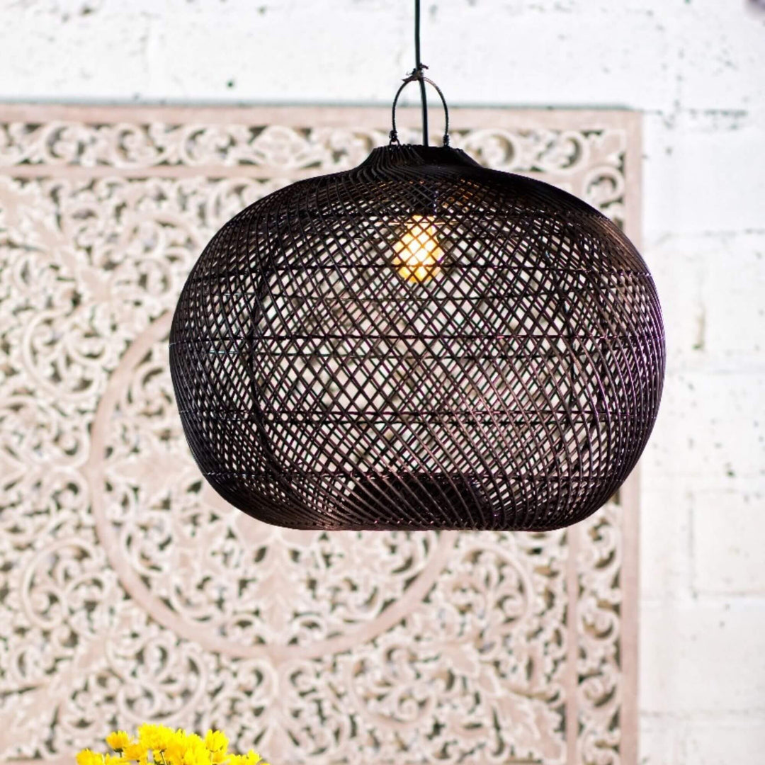 Black rattan Tioman lamp illuminated in a cozy interior setting.