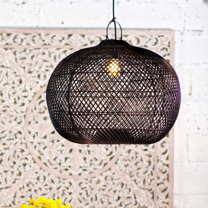 Black rattan Tioman lamp illuminated in a cozy interior setting.