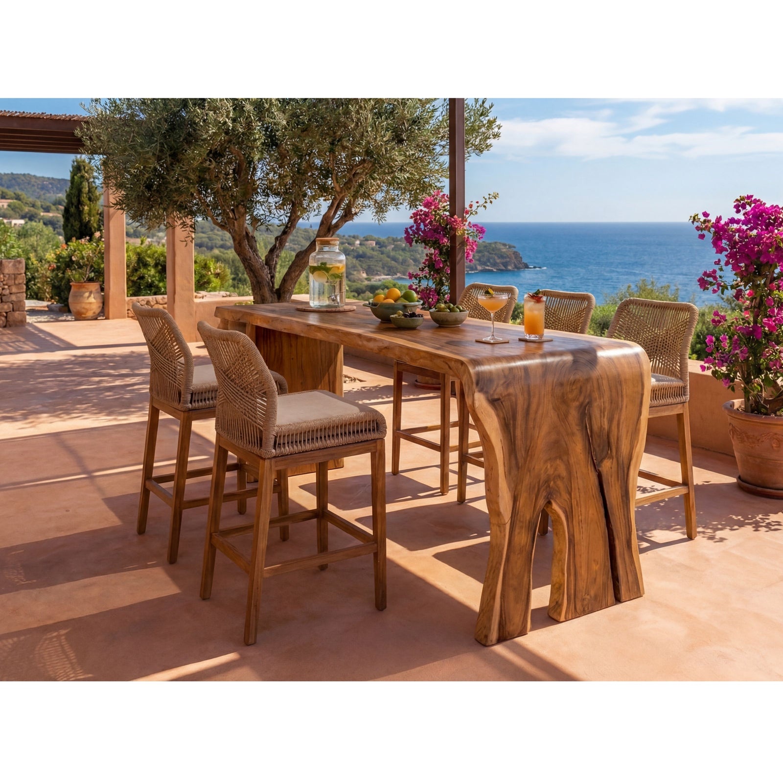 Outdoor bar-height dining set on a sunlit patio overlooking the sea, featuring a rustic wood table with a live-edge front and four woven-back bar stools.