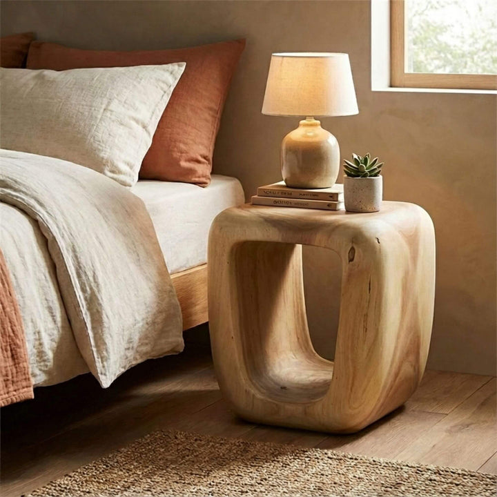 Wooden Trembesi bedside table with lamp and plant next to a bed in a bedroom.
